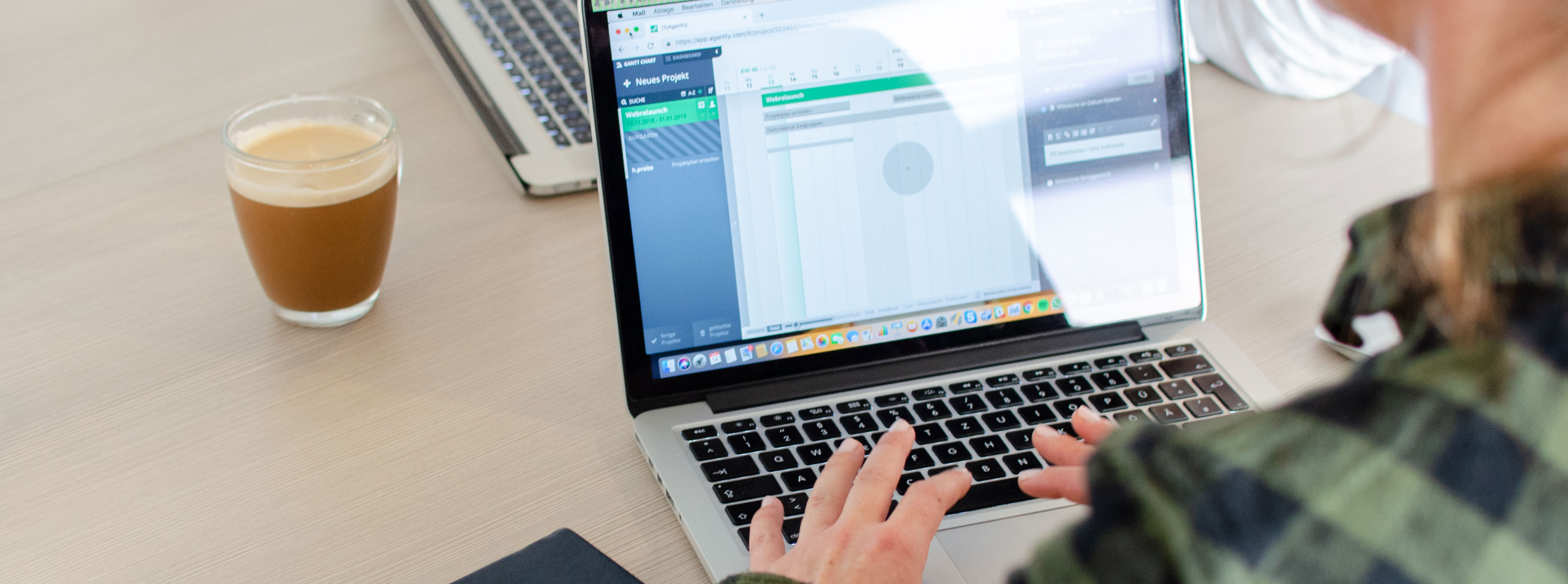 Eine Mitarbeiterin sitzt an ihrem Laptop und arbeitet. Neben ihr steht ein Kaffee.